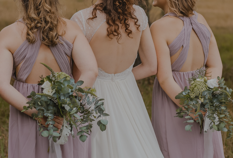 Summer wedding photoshoot inspiration includes bride and bridesmaids holding bouquets from behind