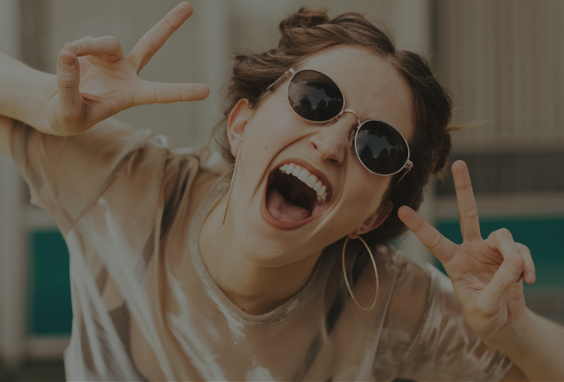 Girl in sunglasses and hoop earrings laughing throwing up the peace sign