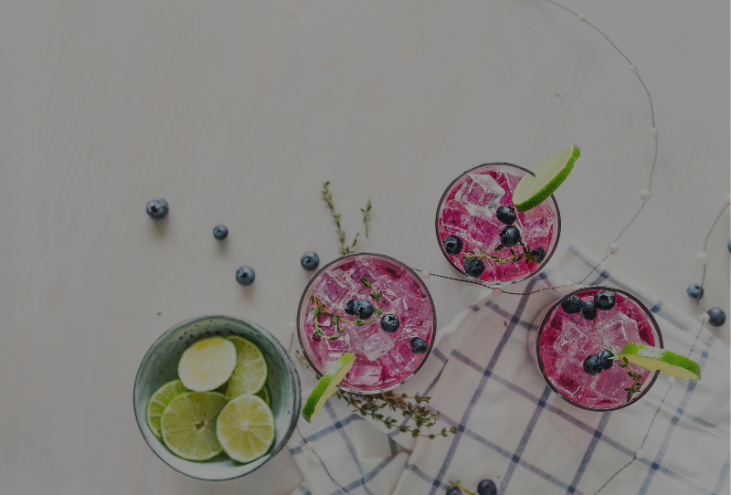 Pink refreshing summer drinks with blueberries and limes on a marble kitchen counter