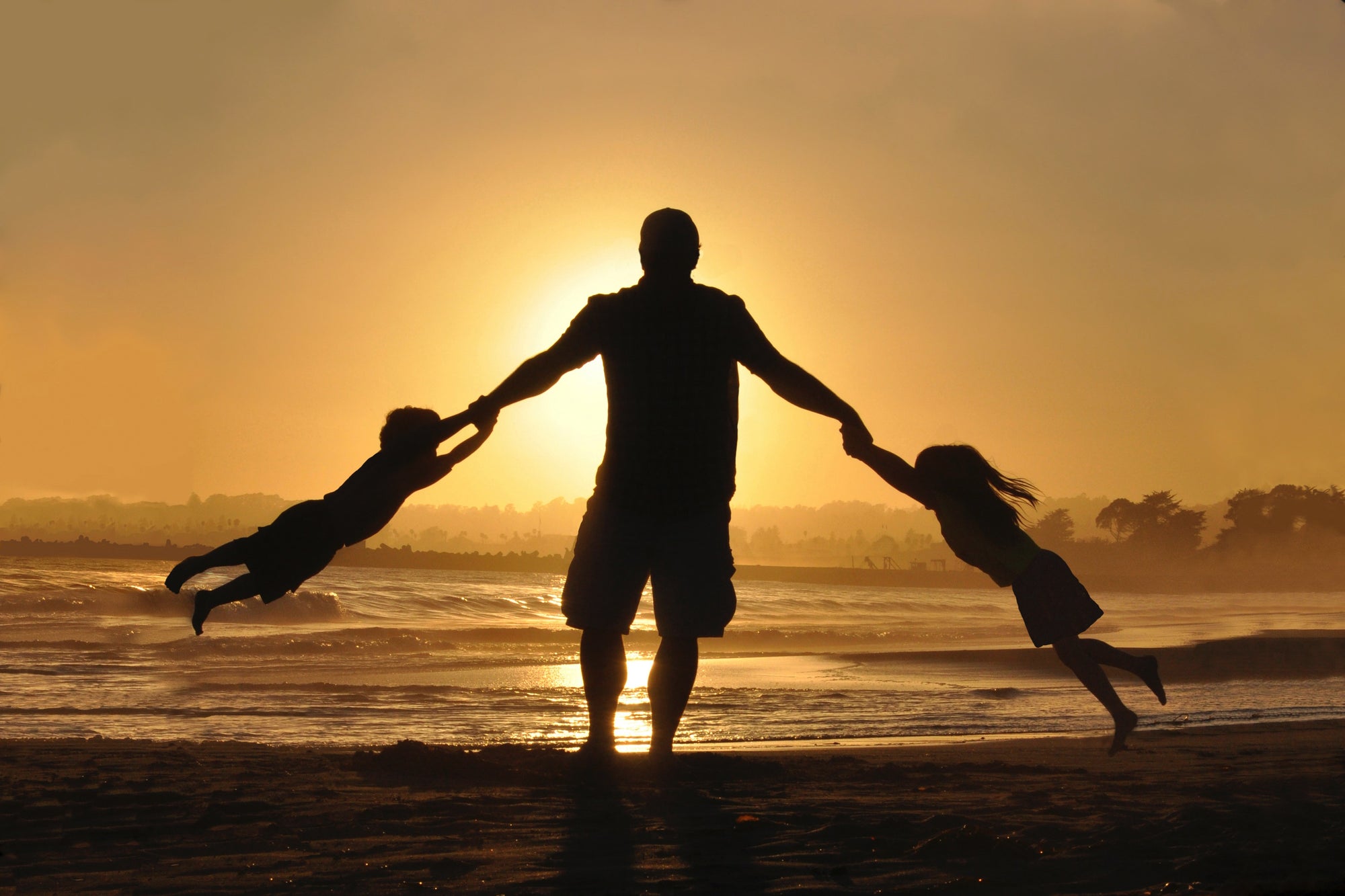 Man on the beach at sundown, swinging his two children in the air