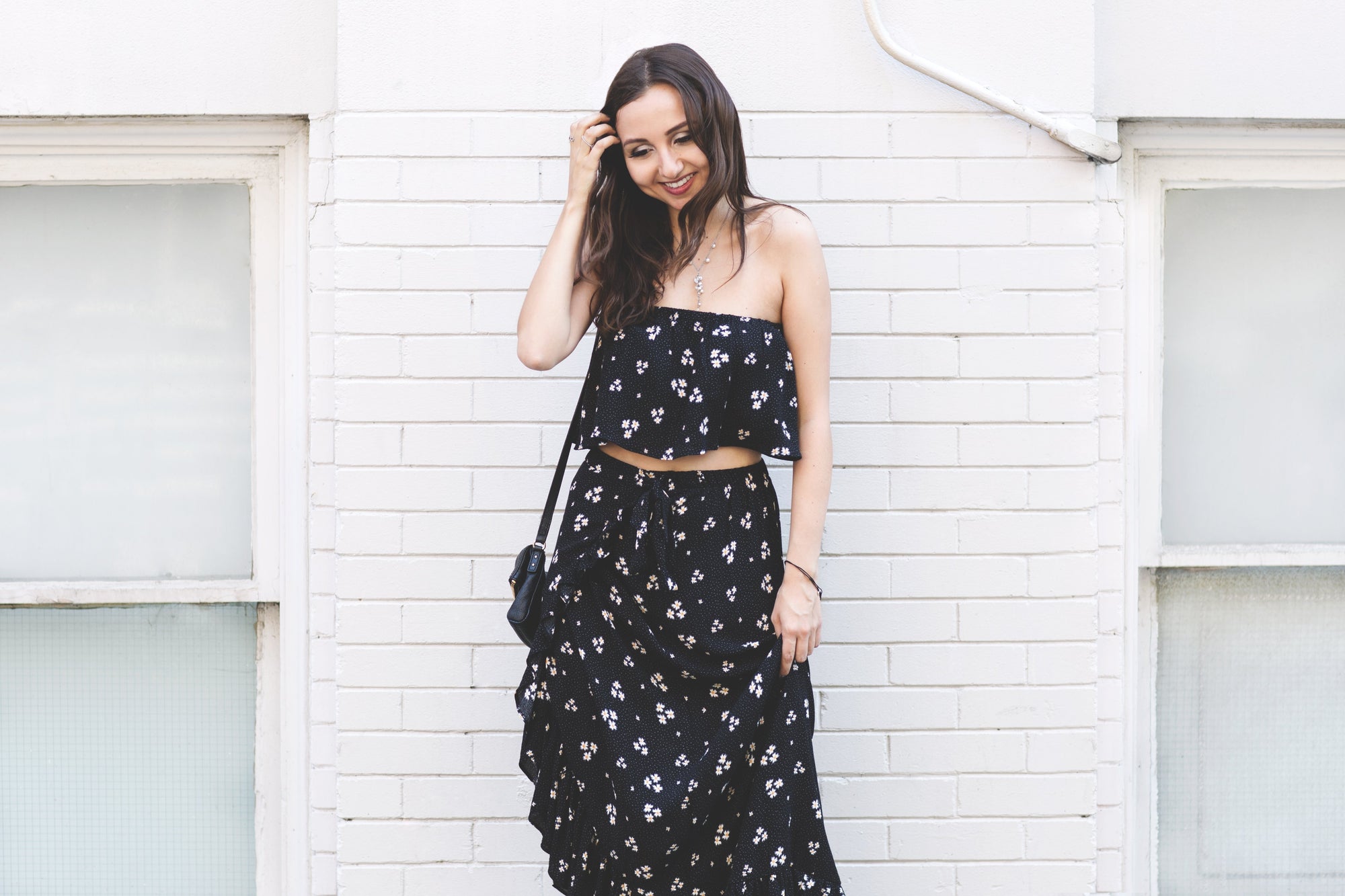 Fashion blogger posing in front of brick wall in floral summer dress with black handbag